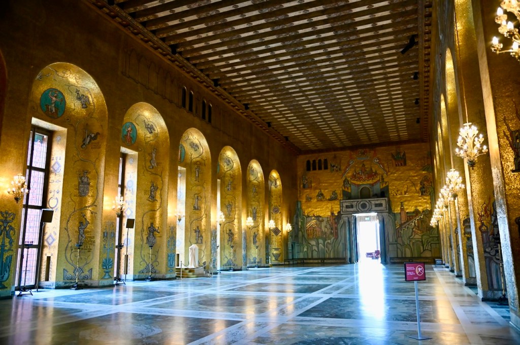 Interior view of the Stockholm City Hall showcasing the Grand Hall with gold leaf decoration, large arched windows, and a wooden ceiling.