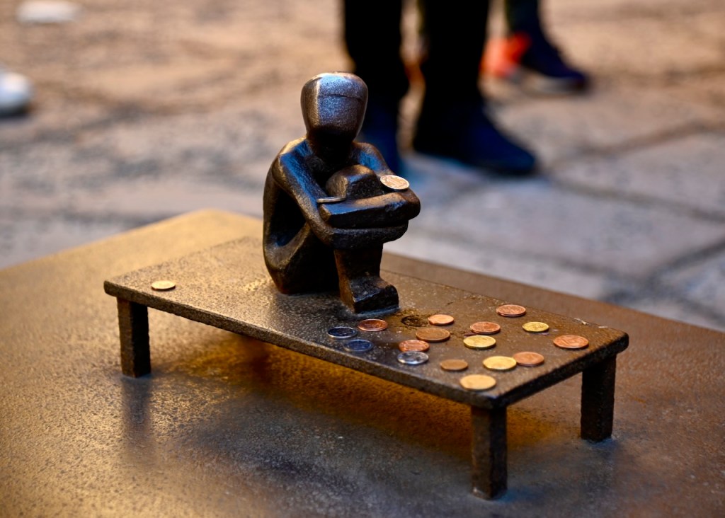 A small bronze sculpture of a seated figure with a contemplative posture, resting on a table with various coins scattered around.