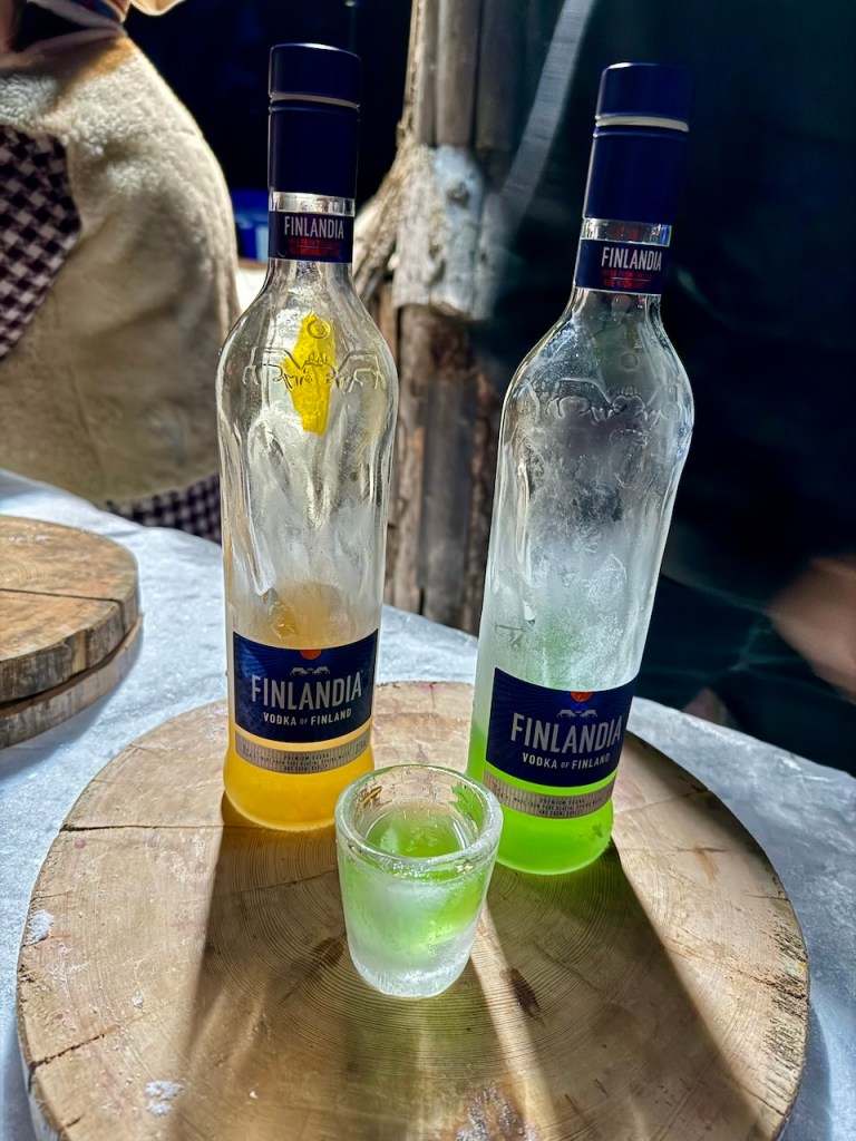 Two bottles of Finlandia vodka on a wooden serving board, one clear and one green, with a shot glass filled with a green liquid in front.