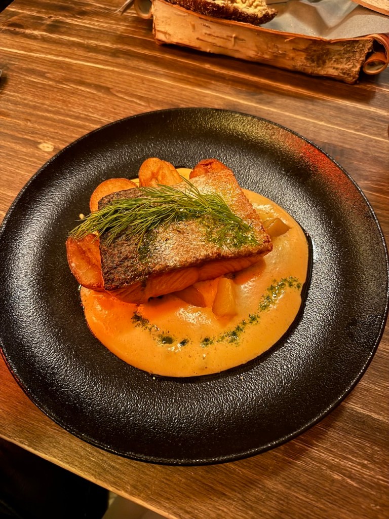 A gourmet dish featuring grilled salmon served on a bed of creamy sauce with fresh herbs and colorful garnishes, presented on a black plate.