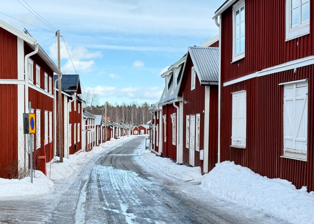 Row of traditional red wooden houses with white trim lining a snowy street in Gammelstad, Sweden.