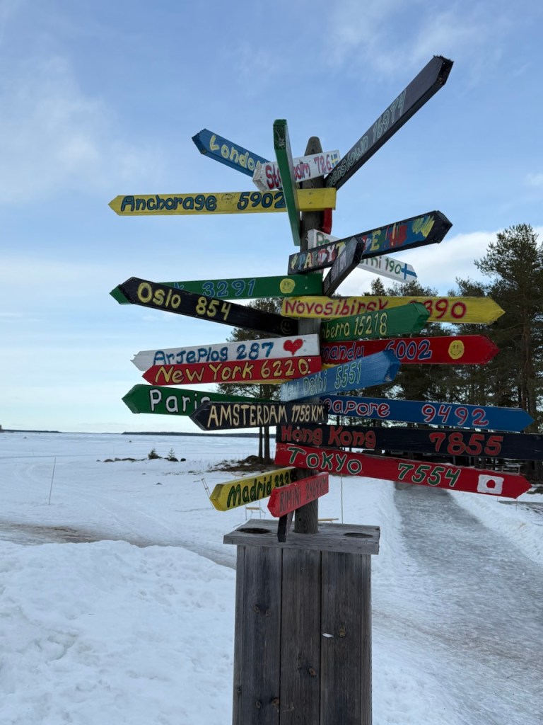 Signpost displaying distances to various cities, including London, New York, and Tokyo, surrounded by snow and trees.