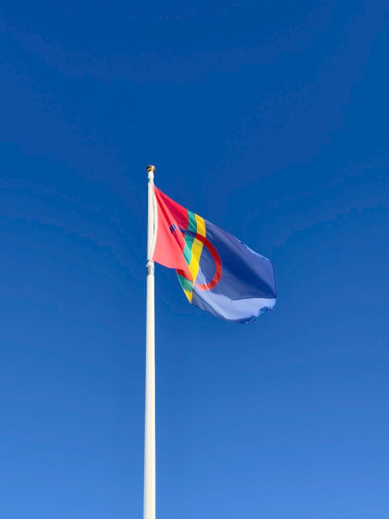 Sami flag waving against a clear blue sky.
