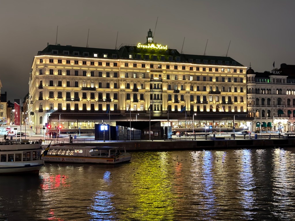 Illuminated exterior of the Grand Hotel in Stockholm, reflecting in the water at night.