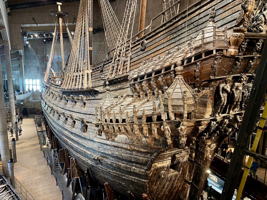 The Vasa ship on display at the Vasa Museum in Stockholm, showcasing its intricate wooden details and masts, surrounded by visitors.