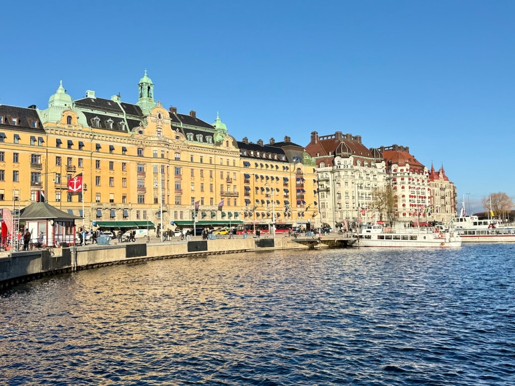 View of colorful buildings along the waterfront in Stockholm, with boats docked and people walking along the promenade.
