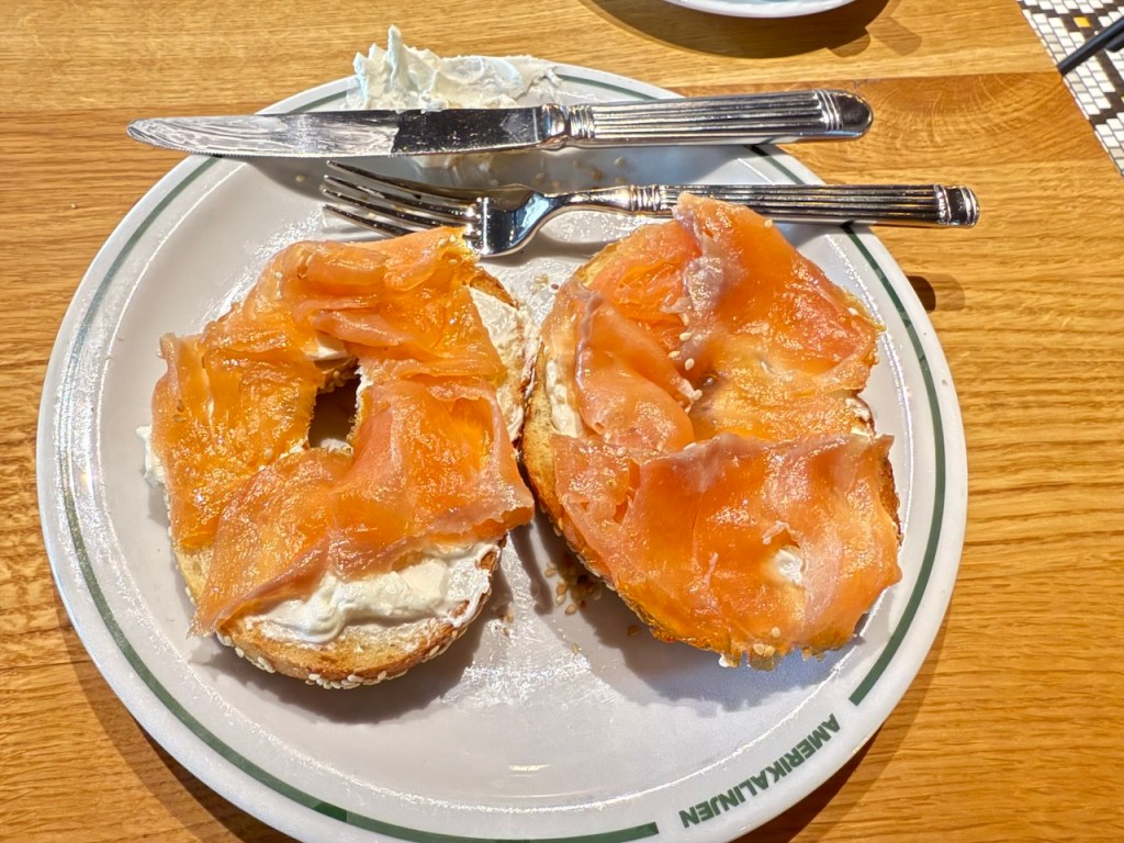 A plate featuring a bagel topped with cream cheese and slices of smoked salmon, accompanied by a knife and fork.