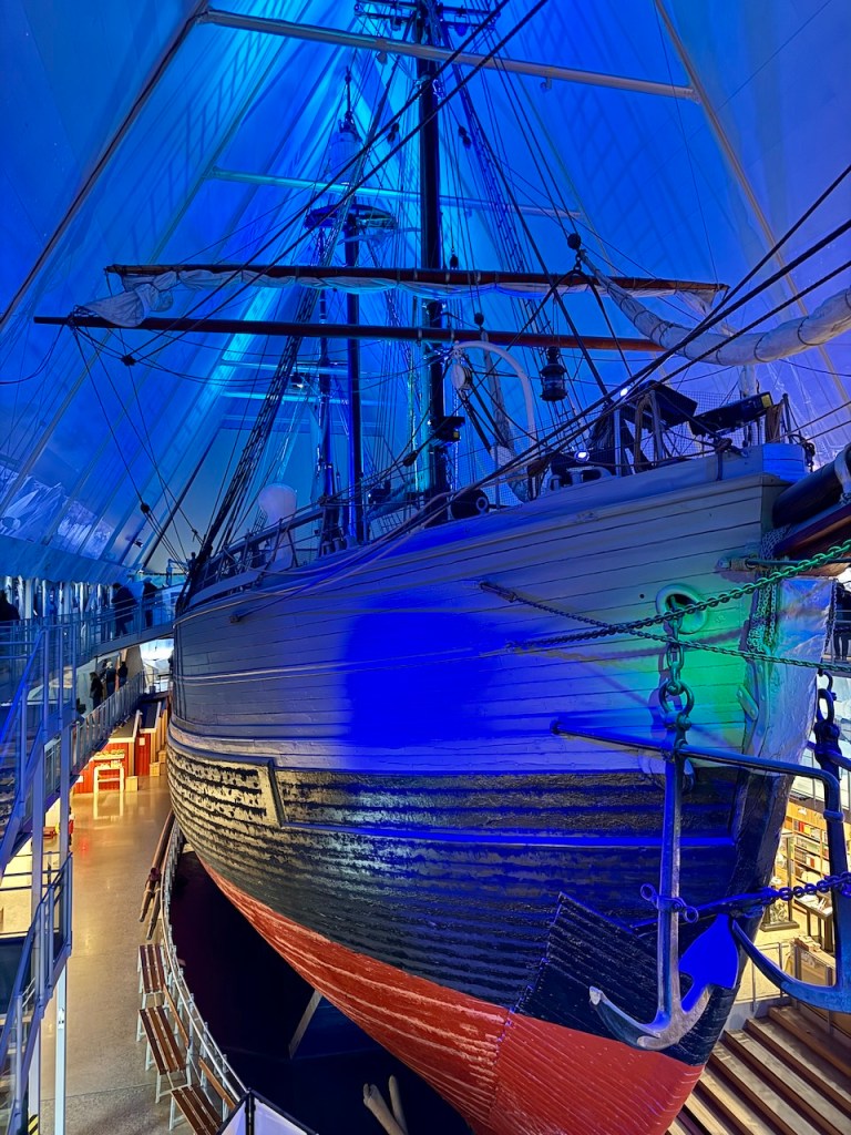 An interior view of the Fram Museum showcasing the famous polar exploration ship, the Fram, illuminated with blue lighting.