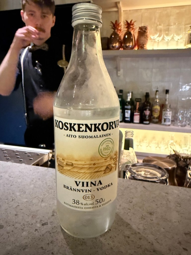 A bottle of Koskenkorva vodka displayed on a bar counter, with a bartender in the background.