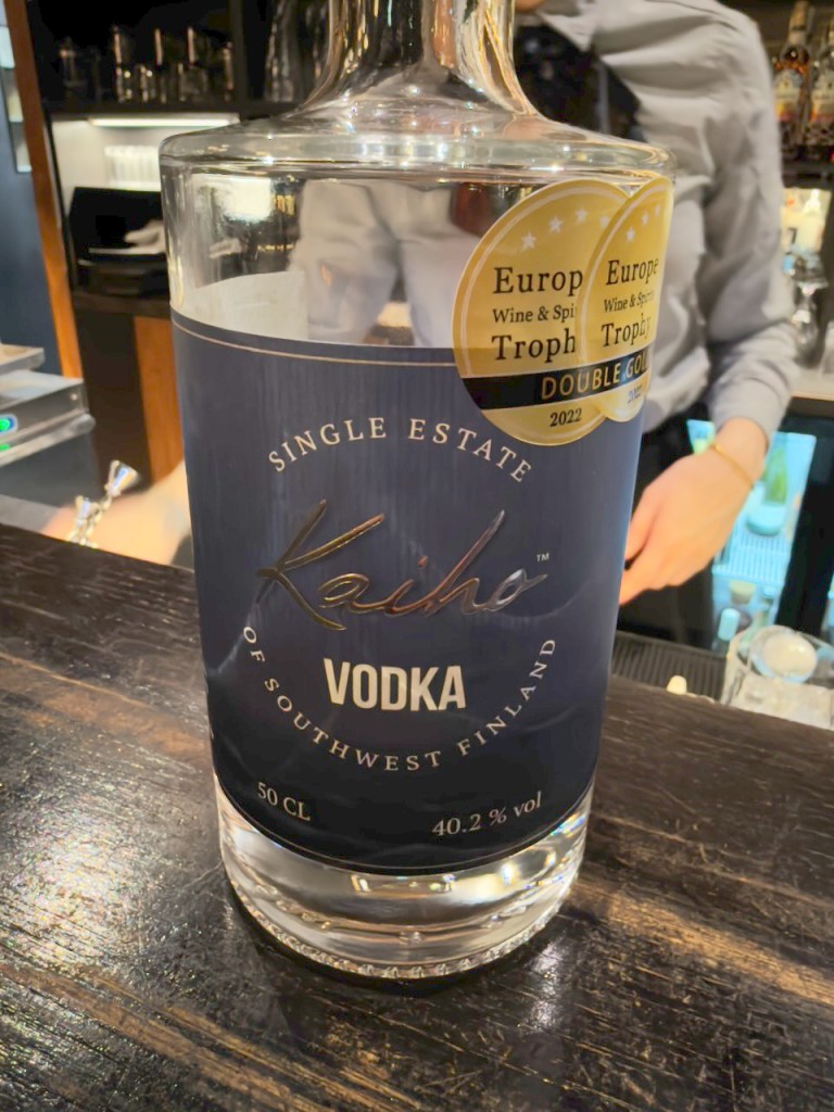 A bottle of Kaiho vodka from Southwest Finland displayed on a wooden bar counter, showcasing its label and award stickers.