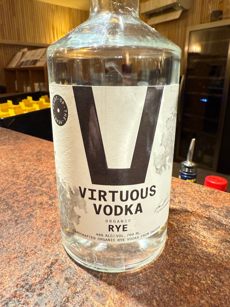 A bottle of Virtuous Vodka, organic rye variety, displayed on a wooden surface with a blurred background.