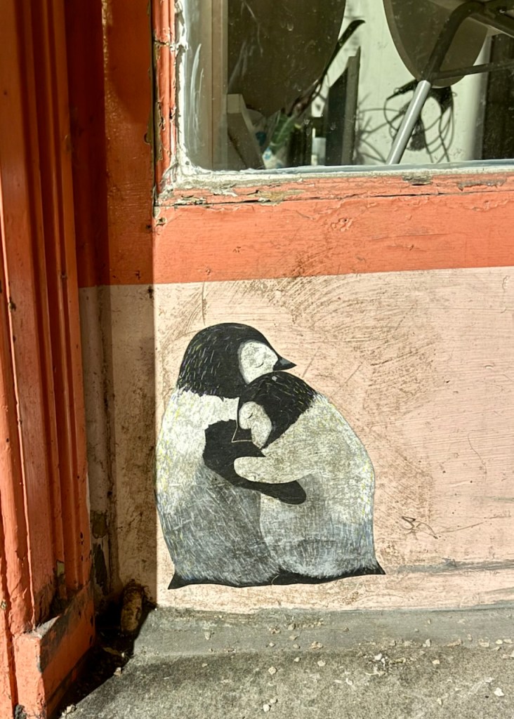 A wall art depicting two penguins embracing, set against a weathered and textured background.