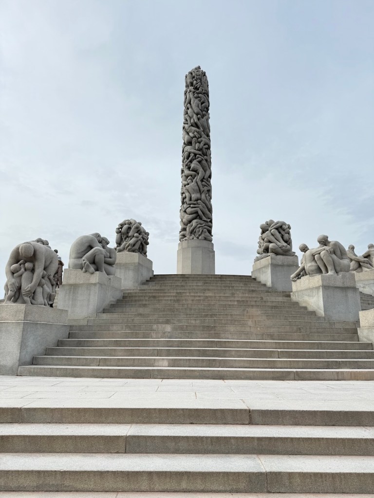 The Monolith at Vigeland Sculpture Park in Oslo, featuring intricate, interwoven human figures carved from granite, ascending a staircase surrounded by other sculptures.