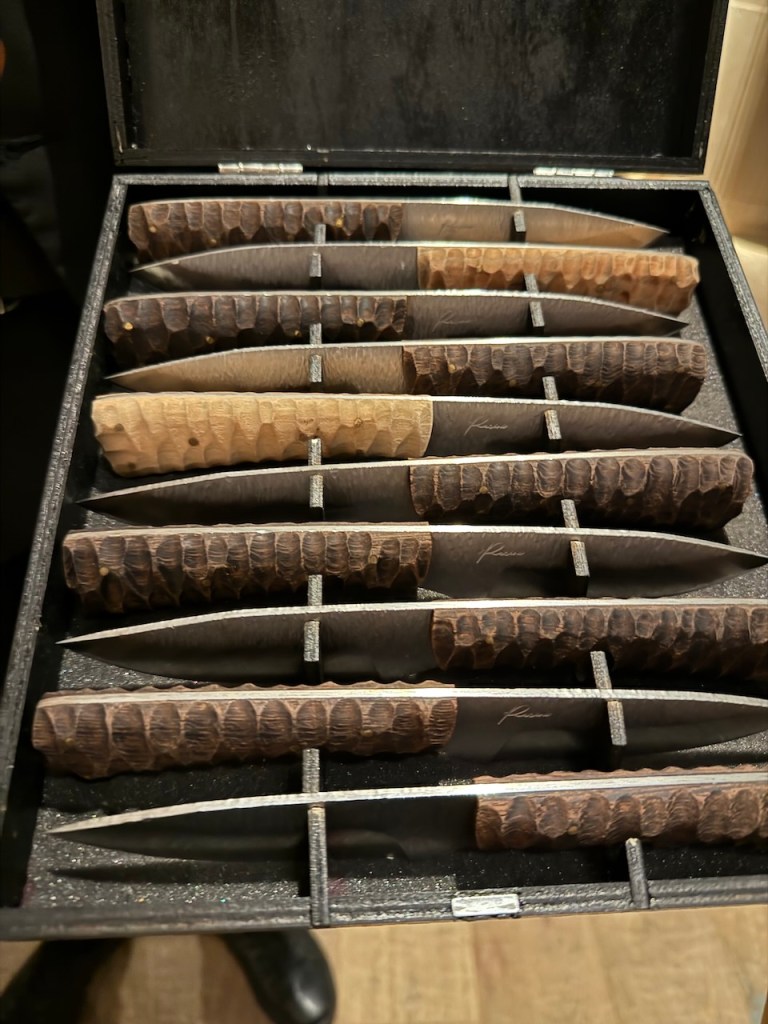 A box containing a selection of beautifully crafted knives with distinct wooden handles, arranged neatly in compartments.