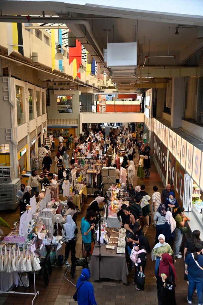 A bustling view of Central Market Kuala Lumpur, showcasing various stalls selling clothing, crafts, and food, with numerous people exploring the market.
