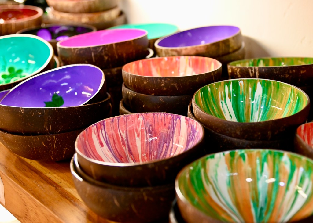 A collection of colorful bowls made from coconut shells, featuring various designs and patterns, displayed on a wooden surface.