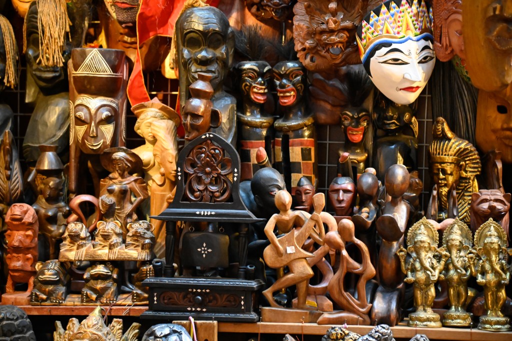 A vibrant display of wooden carvings and masks, showcasing a variety of artistic styles and cultural figures, arranged closely together.