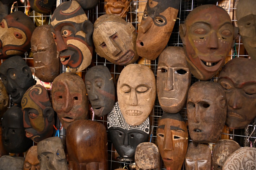 A collection of wooden masks displayed on a grid, showcasing various artistic styles and facial features.
