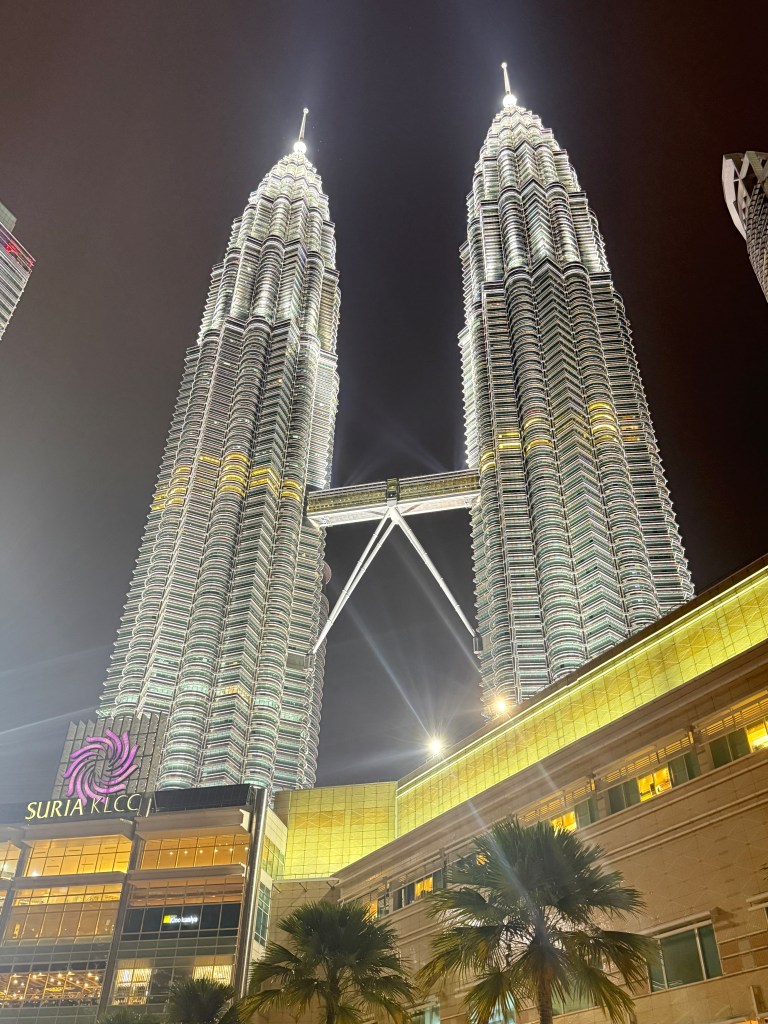 The Petronas Towers illuminated at night, showcasing their architectural features and the Skybridge connecting the two towers.