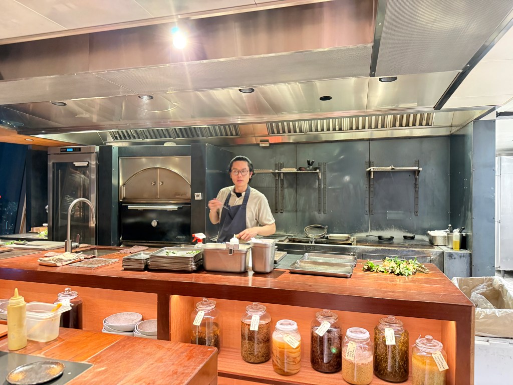 A chef preparing dishes in a modern kitchen, featuring stainless steel appliances and an array of ingredients displayed in glass jars.