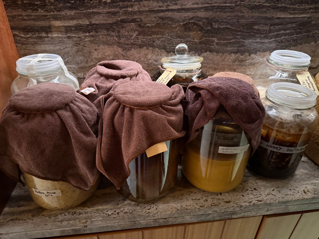 Several jars covered with cloth and labeled with different ingredients, displayed on a countertop.