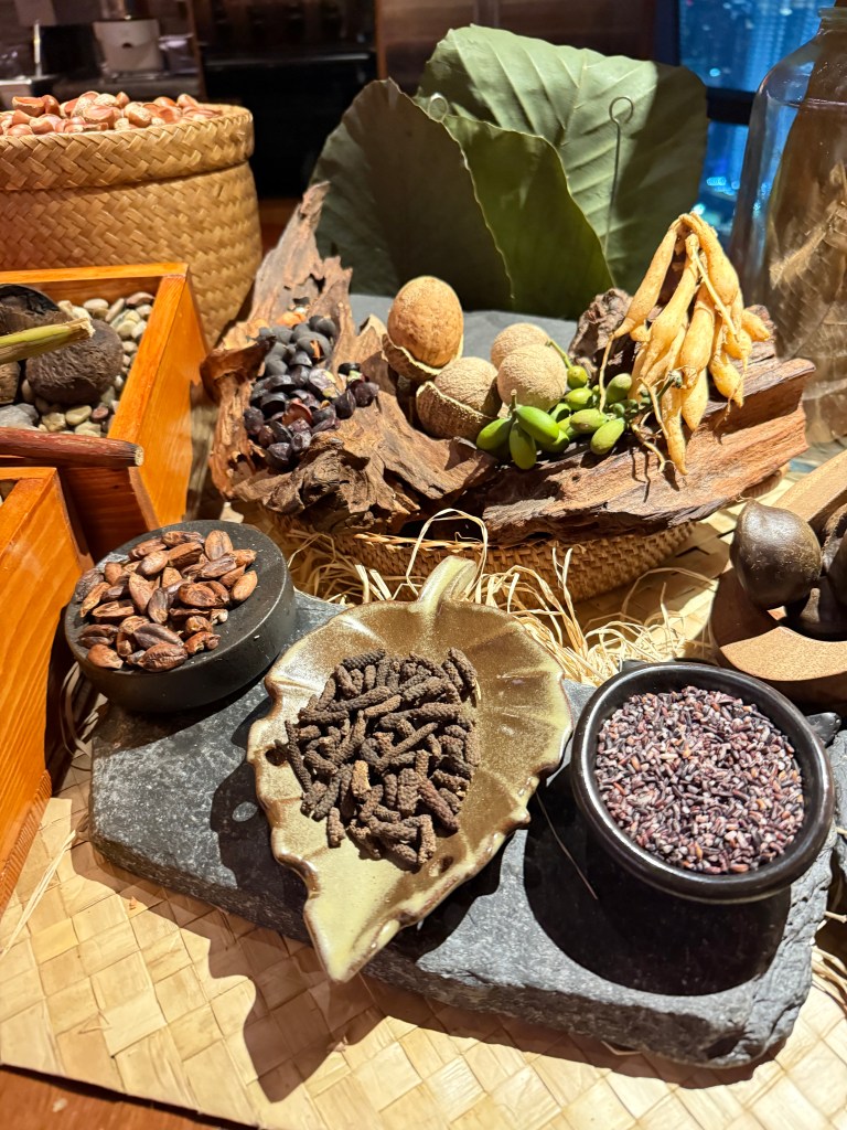 An assortment of spices and local ingredients showcased on a decorative display, featuring cacao beans, various seeds, and colorful spices in bowls and natural elements.