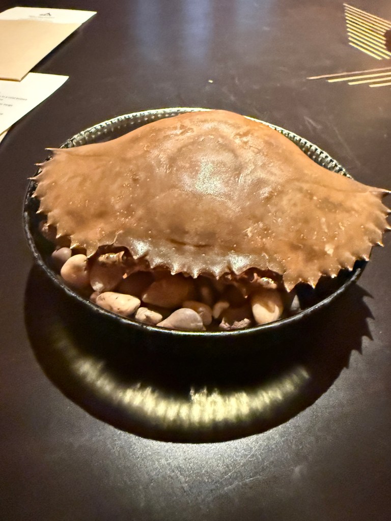 A crab displayed on a plate with some decorative pebbles underneath, set on a dark table.