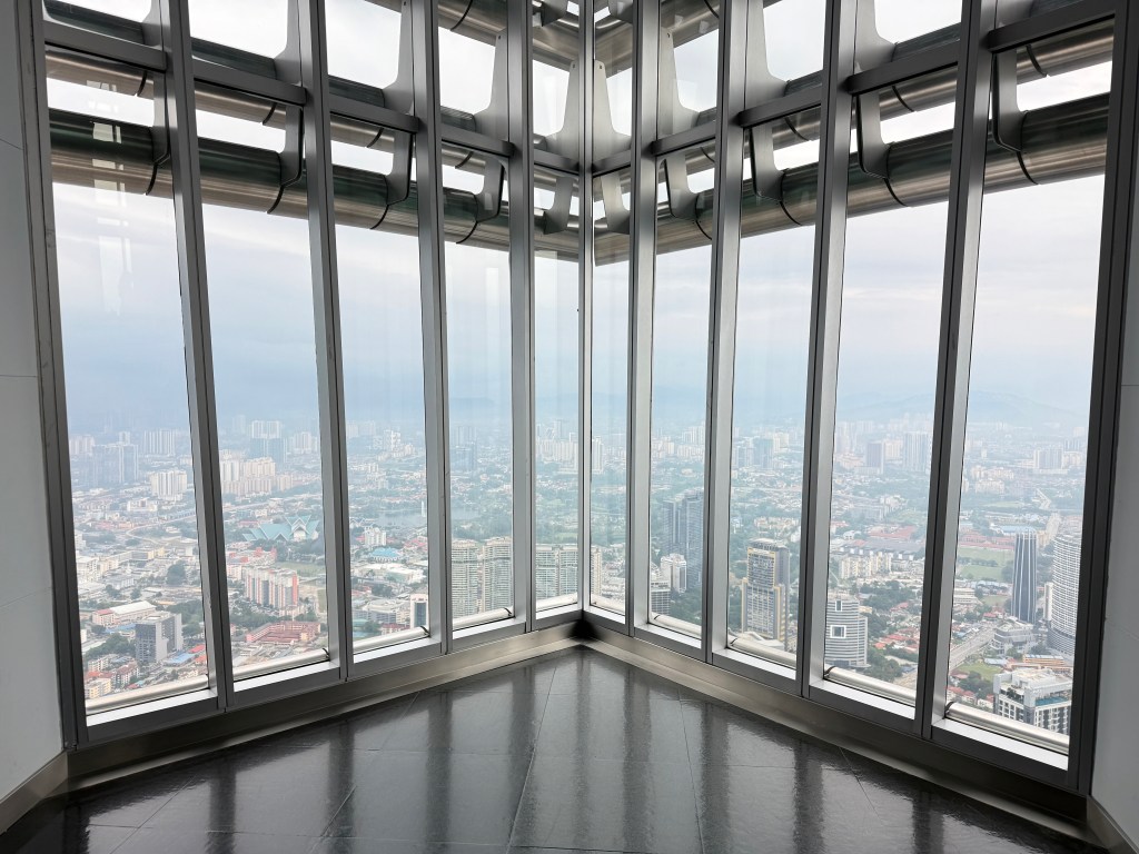 View from the observation deck of the Petronas Towers in Kuala Lumpur, showcasing a panoramic cityscape through large glass windows.
