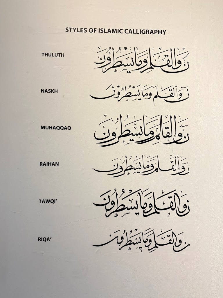 A display showcasing various styles of Islamic calligraphy, including Thuluth, Naskh, Muhaqqaq, Raihan, Tawqi', and Riqa', with examples of each style represented.
