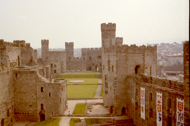 View of a historic castle courtyard surrounded by stone walls and towers, featuring grassy areas and banners hanging on the walls.